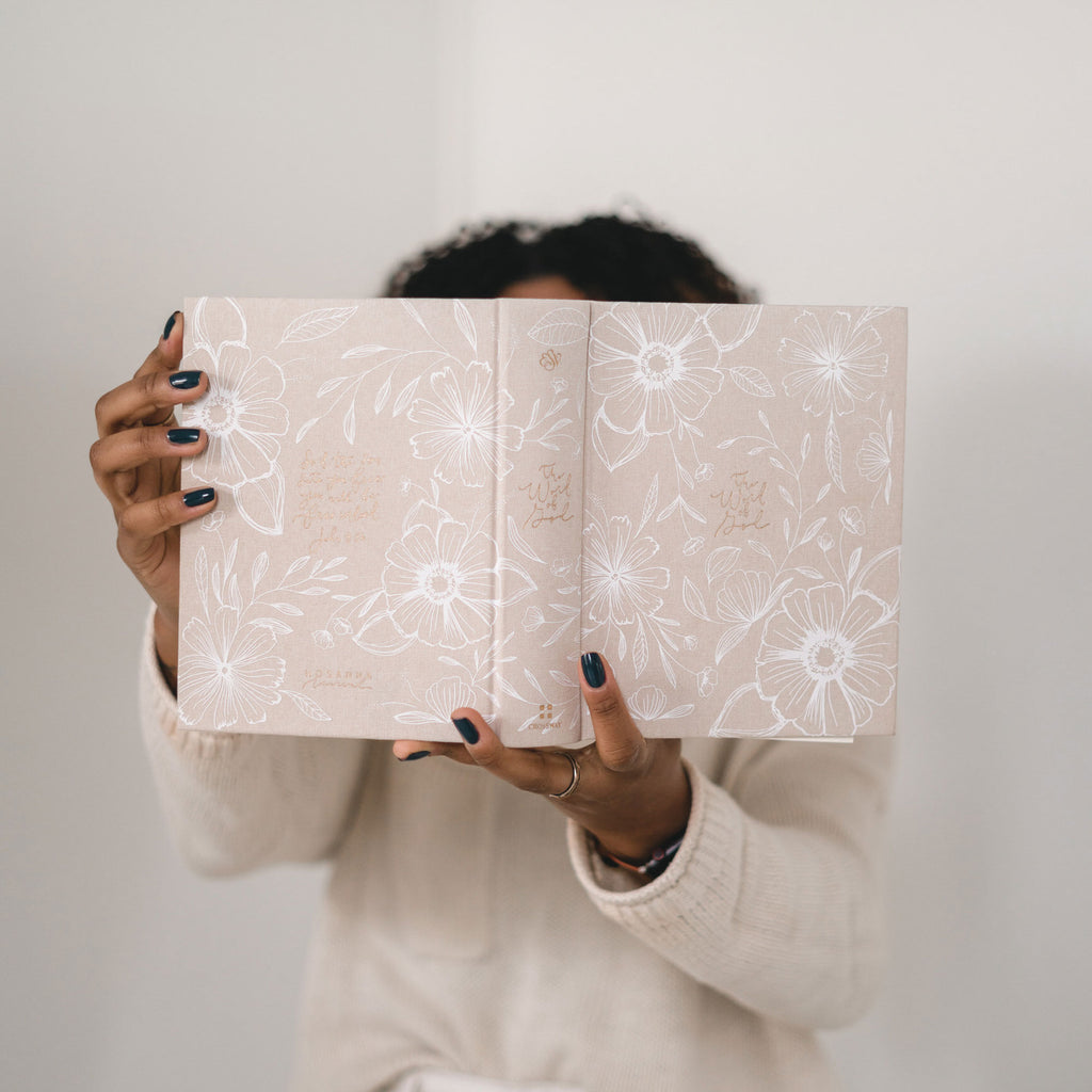 Woman holding open Aesthetic Bible Cover, beige linen with white flowers and gold foil lettering: